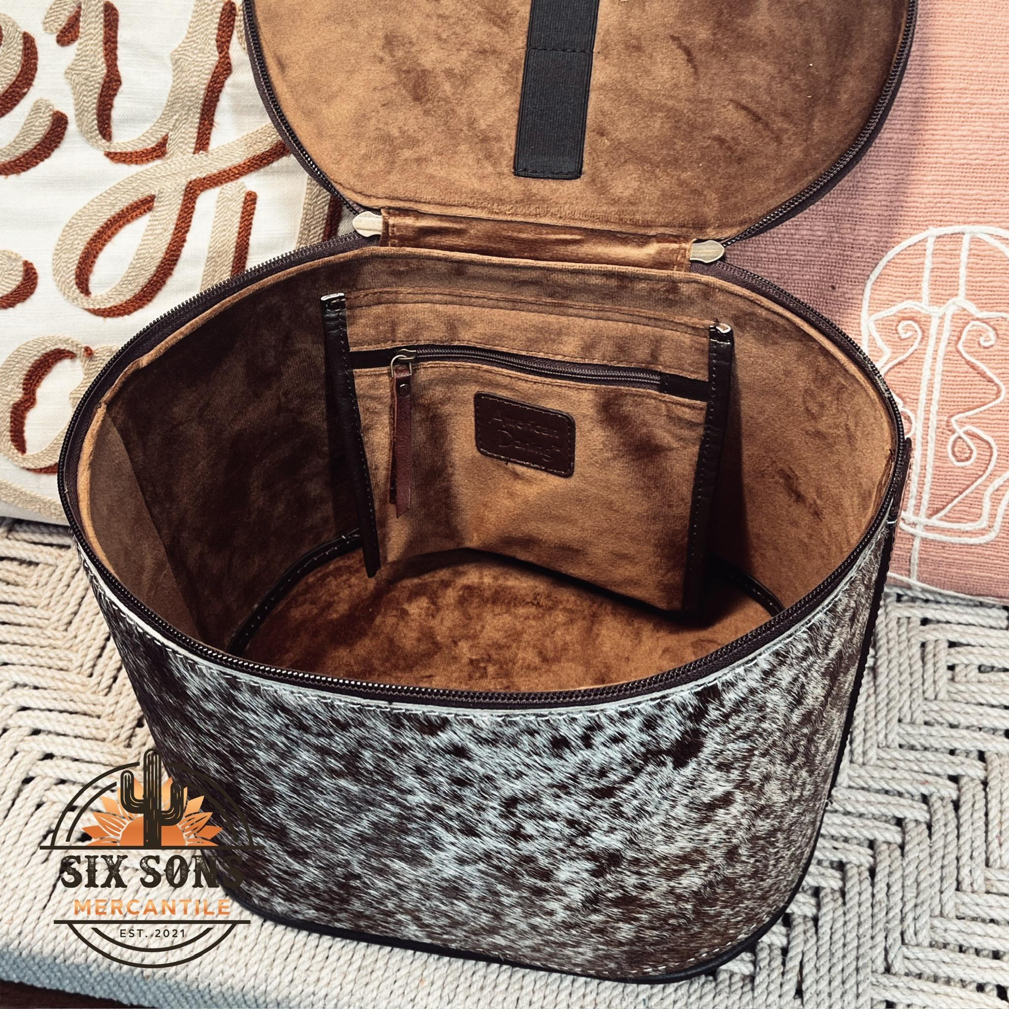 May include: A white and black cowhide round travel bag with a brown leather interior. The bag has a zippered pocket on the inside and a brown leather handle.