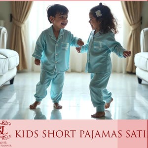 May include: Two children wearing matching light blue satin pajamas with white trim. The pajamas have the word "Mommy" and "Daddy" embroidered on the front. The children are standing on a white tiled floor.