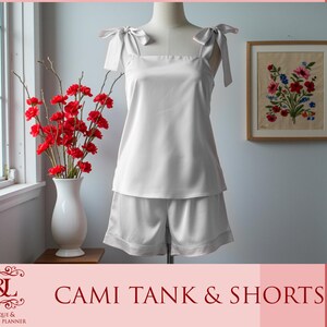 Pu&ograve; includere: Top a canotta e pantaloncini abbinati in satin bianco con sottili spalline. Il top ha una scollatura quadrata e i pantaloncini hanno una cintura larga.