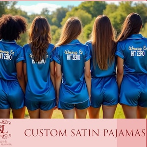May include: Four women wearing matching blue satin pajamas with the text "Wakeup Er Hit Zero" on the back. The pajamas have white piping around the collar and sleeves.
