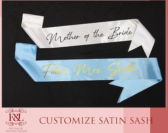 May include: Two satin sashes, one white with black text reading Mother of the Bride and one light blue with gold text reading Future Mrs. Smith. The sashes are displayed horizontally against a black background with text below.