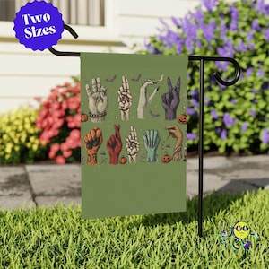 May include: A rectangular garden flag with a sage green background featuring a graphic print of various hands in different colors and positions spelling out the word WITCH, accented with small illustrations of pumpkins, bats, and mushrooms.
