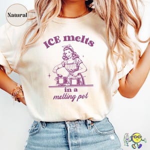 Puede incluir: Camiseta color crema con un gráfico retro en morado. El gráfico presenta a una mujer cocinando con el texto "ICE melts in a melting pot". La camiseta tiene mangas cortas y cuello redondo.