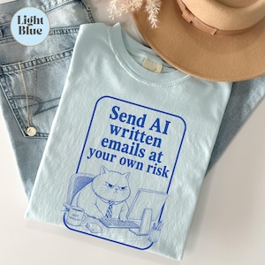 May include: A light blue t-shirt featuring a blue graphic of a grumpy cat sitting at a computer with the text "Send AI written emails at your own risk" and a mug labelled "NOT IMPRESSED" inside a blue rectangular border on the front.