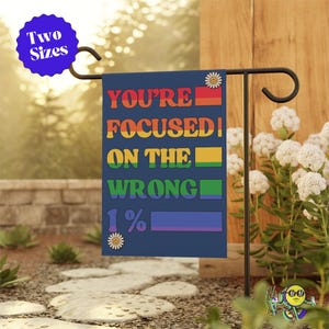 Op de afbeelding: Een blauwe tuin vlag met een regenboogontwerp en de tekst "YOU'RE FOCUSED ON THE WRONG 1%".