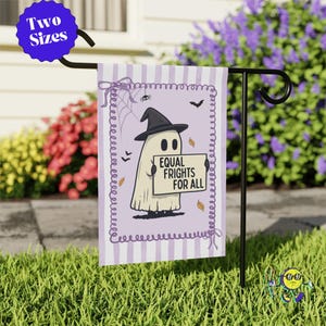 May include: A rectangular garden flag featuring a light purple and white striped background with a decorative border. A ghost wearing a black witch hat holds a sign that reads EQUAL FRIGHTS FOR ALL. The design includes a spider, web, and bats.