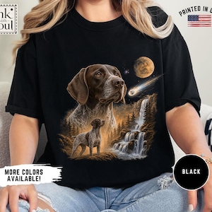 May include: A black t-shirt featuring a graphic print of a brown and white German Shorthaired Pointer dog, a waterfall, a forest, a moon, and a shooting star. The shirt includes the text ink with soul and a small American flag icon.