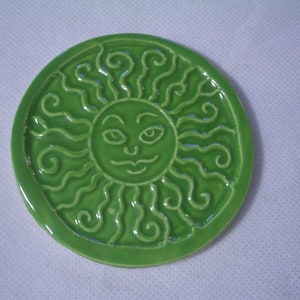 Może przedstawiać: Zielony ceramiczny podkładka pod kubek z wypukłym wzorem uśmiechniętego słońca z kręconymi włosami.
