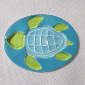 May include: A blue ceramic dish with a green sea turtle design. The turtle is raised and has a textured shell.