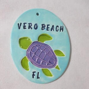 May include: A light blue ceramic ornament featuring a purple sea turtle and the text "VERO BEACH FL".