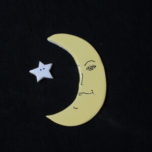 May include: A yellow crescent moon with a face drawn on it and a white five-pointed star with two black dots.