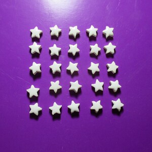 May include: Twenty-eight small, white star-shaped objects arranged in a grid pattern against a solid purple background. The stars have a slightly rounded, three-dimensional appearance.