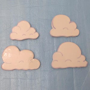 May include: Four cloud-shaped wooden cutouts. Each cloud is painted white with a light purple outline. The clouds are arranged on a light blue textured surface.