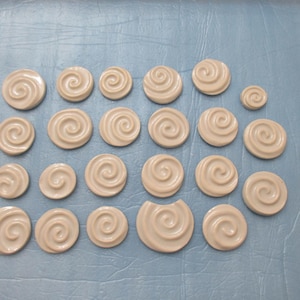 Puede incluir: Colección de piezas de cerámica blanquecina con diseño de espiral, de varios tamaños. Las piezas están dispuestas sobre una superficie azul claro. Cada pieza presenta un diseño de espiral central.