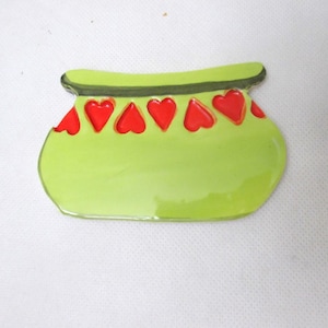 May include: A lime green ceramic dish shaped like a wide bowl with a flat top edge. The upper section features a horizontal dark green band decorated with a row of six bright red heart-shaped indentations across the front surface.