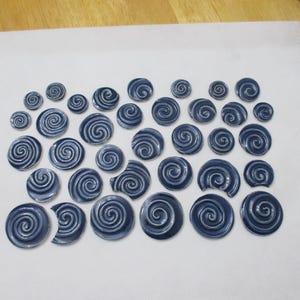 Puede incluir: Colección de elementos decorativos en espiral azul oscuro, dispuestos sobre una superficie blanca. Los elementos, de tamaños variados y con acabado brillante, crean un efecto texturizado. El diseño evoca formas orgánicas.