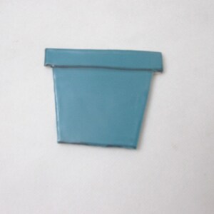 Peut inclure: Un pot de fleurs bleu sarcelle avec une finition lisse et brillante et un rebord large et plat. Le récipient présente une forme trapézoïdale effilée qui se rétrécit vers la base, offrant une surface unie et propre sans aucun motif ni texture.