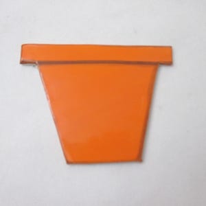 Könnte beinhalten: Ein leuchtend orangefarbenes, flaches, trapezförmiges Objekt mit einem breiten, horizontalen Rand an der Oberseite. Die Oberfläche wirkt glatt und glänzend und weist durchgehend eine kräftige, einheitliche orange Farbe auf, die an einen Blumentopf erinnert.