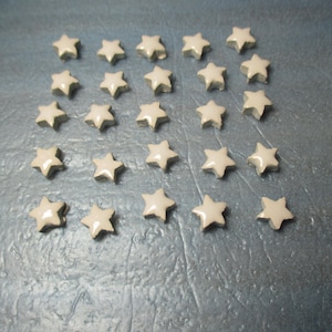 Puede incluir: Una colección de 25 azulejos de cerámica blanca en forma de estrella. Los azulejos están dispuestos en una cuadrícula sobre una superficie azul.