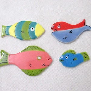 May include: Four colorful ceramic fish figurines. One is yellow and green, another is red and blue, a third is pink and green, and the last is blue and green. Each fish has a unique design and expression, perfect for home decor.