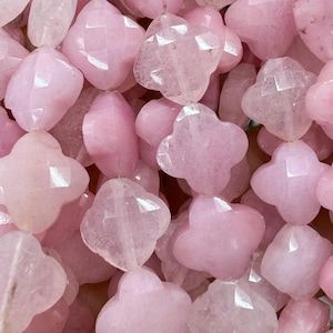 Könnte beinhalten: Nahaufnahme eines Stapels rosa, facettierter Edelsteinperlen. Die Perlen sind in Form eines vierblättrigen Kleeblatts.