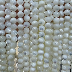 Peut inclure: Gros plan sur des brins de perles blanches et rondes. Les perles ont un éclat nacré et sont enfilées ensemble, créant un aspect fluide et texturé. Les perles sont de taille et de forme uniformes, idéales pour la bijouterie.