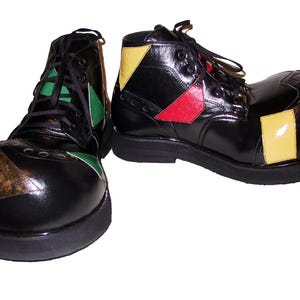 Puede incluir: Un par de botas negras con cordones y un diseño de punta redondeada de gran tamaño. Las botas tienen un acabado brillante con parches geométricos en contraste de colores amarillo, rojo, verde y marrón. Cada bota tiene una suela negra gruesa.