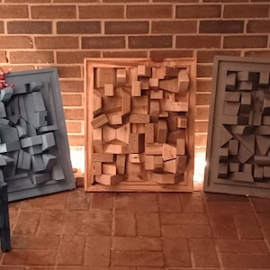 Może przedstawiać: Trzy kwadratowe obrazy ścienne o geometrycznym wzorze. Obrazy wykonane są z drewna i pomalowane w odcieniach niebieskiego, brązowego i szarego.