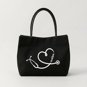 May include: Black tote bag with a white stethoscope design forming a heart shape, with the word "custom" in script. The bag has black handles and is likely made of canvas or a similar material. The design is simple and clean.