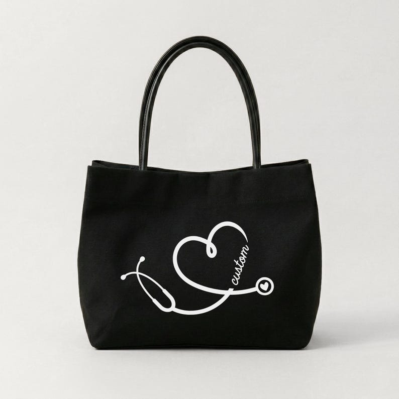 May include: Black tote bag with a white stethoscope design forming a heart shape, with the word "custom" in script. The bag has black handles and is likely made of canvas or a similar material. The design is simple and clean.