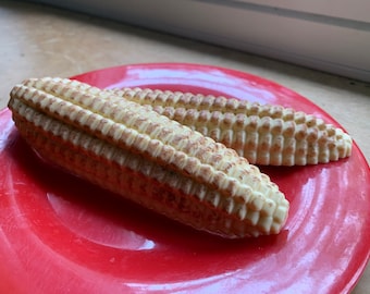 May include: Two white chocolate corn on the cob on a red plate.