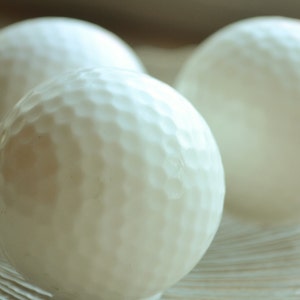 May include: Three white golf balls with a dimpled surface.