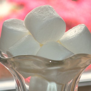 Puede incluir: Un bol de vidrio lleno de malvaviscos blancos. El bol es transparente y tiene un borde ondulado. Los malvaviscos son suaves y esponjosos.