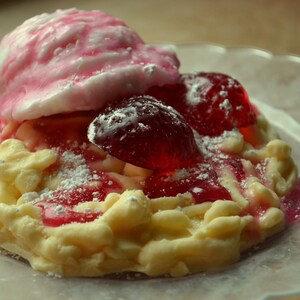 May include: A white and yellow dessert topped with pink and red candy, dusted with powdered sugar.