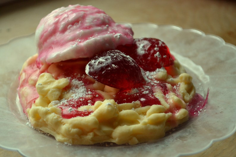 May include: A white and yellow dessert topped with pink and red candy, dusted with powdered sugar.