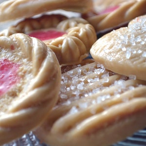 Könnte beinhalten: Nahaufnahme einer Auswahl an Keksen, darunter herzförmige Kekse mit Zuckerkristallen, runde Kekse mit rosa Zuckerguss und Wirbelkekse mit hellem braunen Guss.
