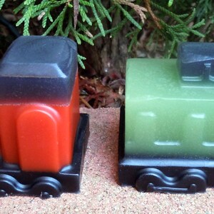 May include: Two toy train engines made of soap. One is red with a black top and the other is green with a black top.