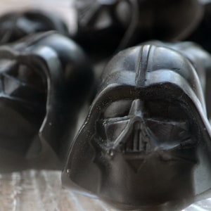 Puede incluir: Un grupo de caramelos de chocolate negro con forma de casco de Darth Vader.