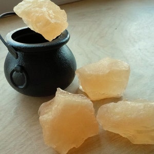 Puede incluir: Cuatro piezas de caramelo de roca naranja translúcidas junto a un caldero negro con asa.