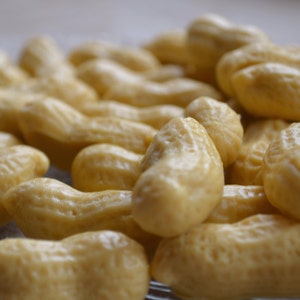 Pode incluir: Um close-up de uma tigela cheia de doces em forma de amendoim. Os doces s&atilde;o de cor castanho claro e t&ecirc;m um acabamento liso e brilhante.