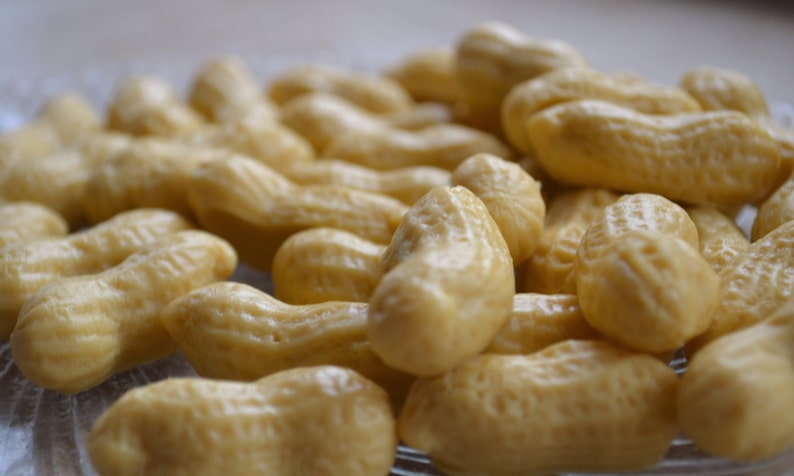 Pode incluir: Um close-up de uma tigela cheia de doces em forma de amendoim. Os doces s&atilde;o de cor castanho claro e t&ecirc;m um acabamento liso e brilhante.