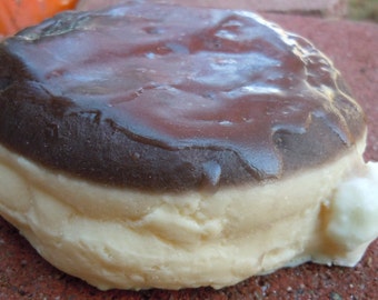 May include: A chocolate-covered donut with a white cream filling. The donut is glazed with a dark chocolate icing and has a slightly irregular shape.