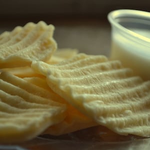 May include: A close-up of a plate of crispy, golden-brown potato chips with a small white plastic container of milk in the background.