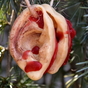 May include: A close-up of a beige and red ear-shaped object hanging from a tree branch. The object is made of a soft, pliable material and has a textured surface. The object is decorated with red accents and appears to be a handmade ornament.