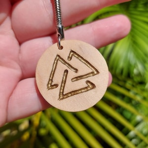 May include: A wooden keychain with a gold-colored triple triangle symbol. The keychain is round and has a silver chain attached.