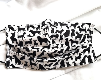 May include: A white face mask with a repeating pattern of black dog silhouettes. The mask has black elastic ear loops and is made of a pleated fabric. The dogs are in various poses and sizes.