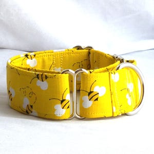 May include: A bright yellow fabric collar featuring a repeating pattern of black and white bees. The collar includes a silver-toned metal D-ring for attachment and a matching metal slide adjuster to modify the length of the strap for a secure fit.