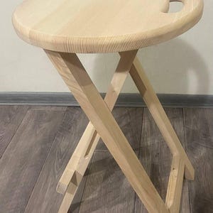 May include: A light wood folding table with a round top and a cutout handle. The table has a simple, rustic design and is perfect for small spaces.