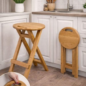 May include: Two wooden folding stools. One is open, showing a round seat and a cross-legged base. The other is folded, revealing the handle on the seat. The stools are made of light-coloured wood.