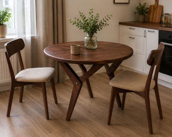 May include: A round, dark brown wooden dining table with two matching chairs. The chairs have light beige upholstered seats and curved backs. A glass vase with greenery and a mug sit on the table.